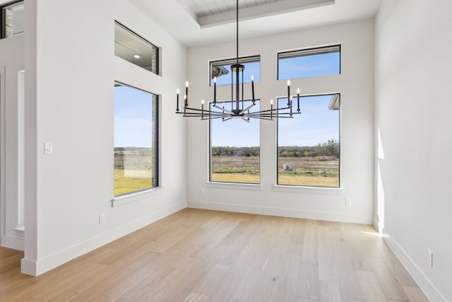 unfurnished dining area with light wood-type flooring, a tray ceiling, and a notable chandelier