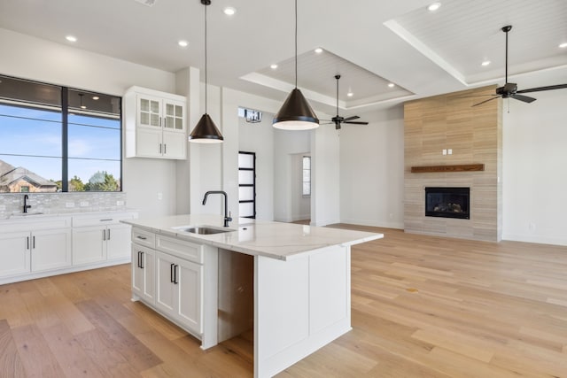 kitchen with white cabinets, a raised ceiling, sink, light stone countertops, and light hardwood / wood-style floors