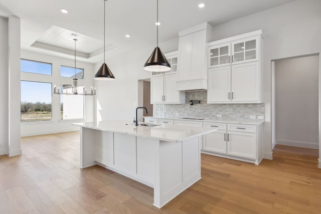 kitchen with light hardwood / wood-style flooring, white cabinetry, a tray ceiling, and sink