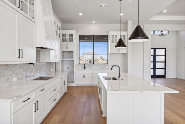 kitchen with pendant lighting, a center island with sink, sink, light hardwood / wood-style floors, and white cabinetry