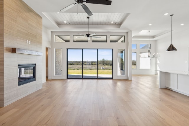 unfurnished living room featuring a fireplace, a towering ceiling, light wood-type flooring, and a raised ceiling