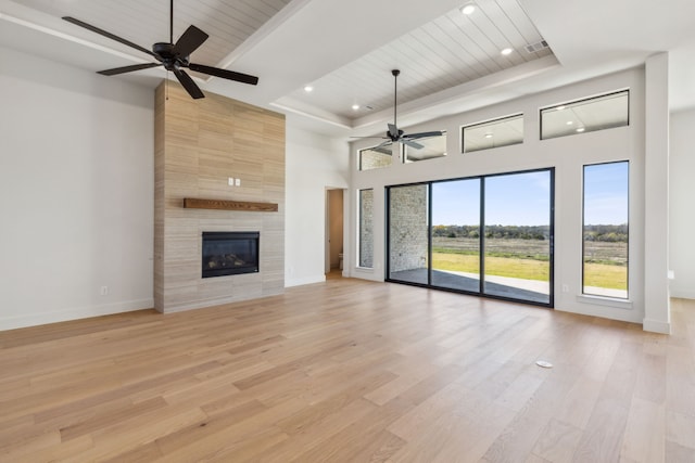 unfurnished living room featuring a high ceiling, light hardwood / wood-style floors, ceiling fan, and a tiled fireplace