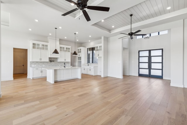 unfurnished living room with a tray ceiling, ceiling fan, a towering ceiling, and light wood-type flooring