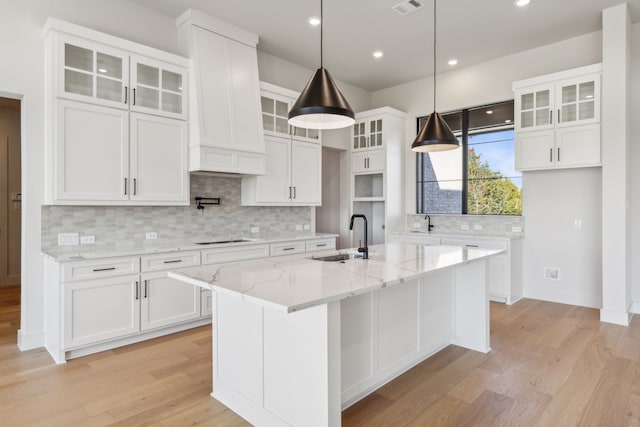 kitchen featuring a kitchen island with sink, sink, white cabinets, and light stone countertops