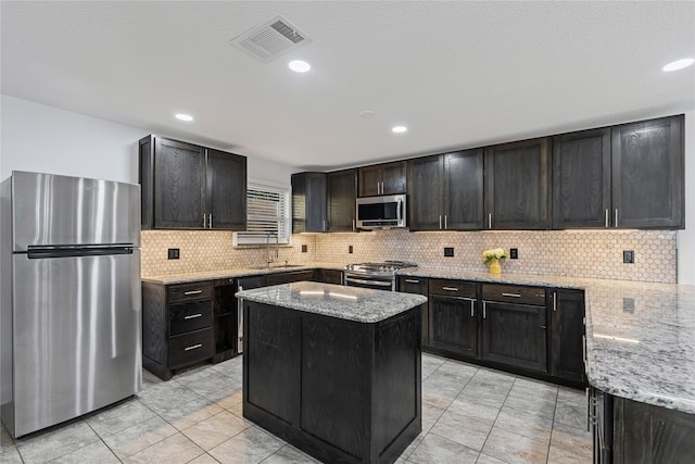 kitchen with a kitchen island, light stone countertops, stainless steel appliances, and tasteful backsplash