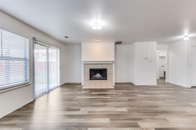 unfurnished living room featuring visible vents, a tiled fireplace, light wood-style flooring, and baseboards