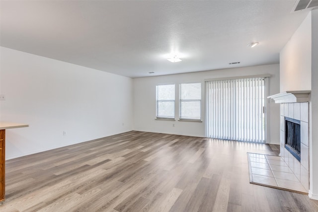 unfurnished living room with light wood-type flooring, a textured ceiling, and a tile fireplace