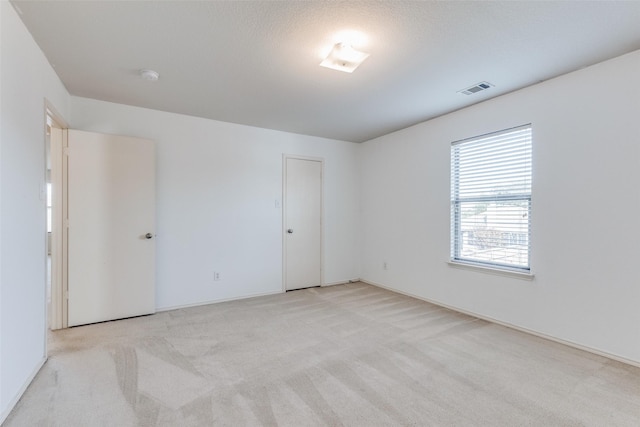 empty room with visible vents, a textured ceiling, and light colored carpet