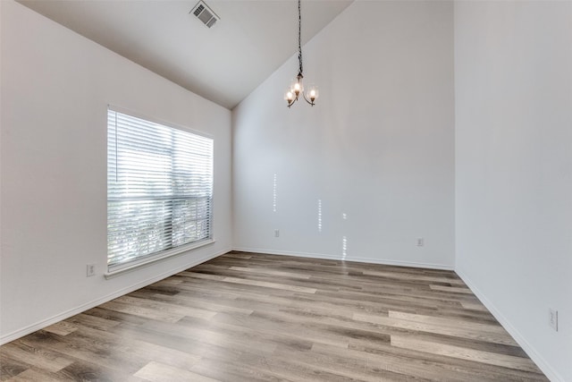 empty room with light hardwood / wood-style floors, high vaulted ceiling, and an inviting chandelier