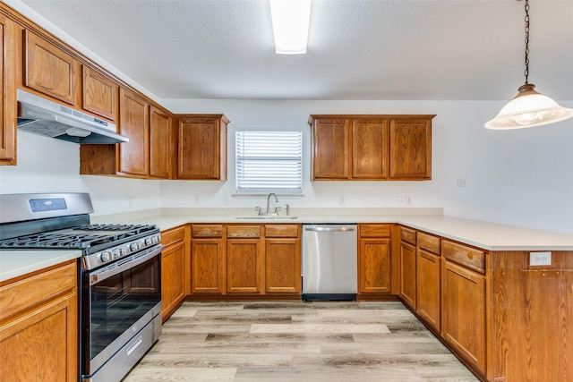 kitchen featuring light wood-type flooring, stainless steel appliances, sink, decorative light fixtures, and range hood