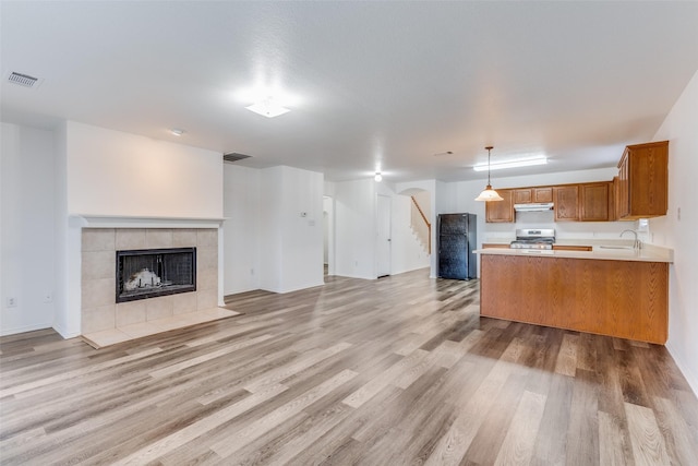 kitchen featuring visible vents, brown cabinetry, a tile fireplace, open floor plan, and under cabinet range hood