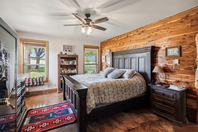 bedroom with a fireplace, ceiling fan, and wood walls