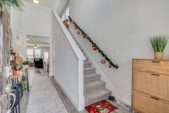 stairway featuring a towering ceiling and ceiling fan