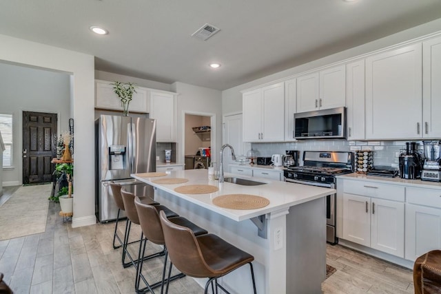 kitchen featuring white cabinetry, sink, a breakfast bar, a center island with sink, and appliances with stainless steel finishes