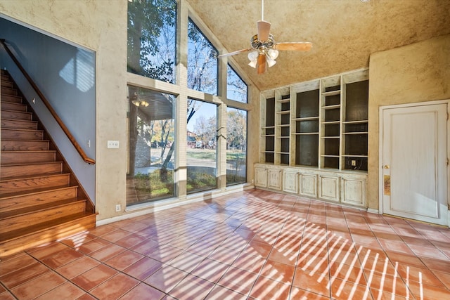 unfurnished living room with ceiling fan, built in shelves, tile patterned floors, and a towering ceiling