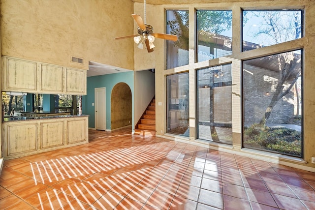 interior space with ceiling fan, tile patterned flooring, a towering ceiling, and light brown cabinets