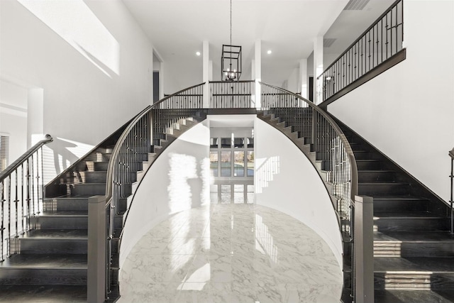 staircase featuring recessed lighting, a notable chandelier, marble finish floor, and a towering ceiling