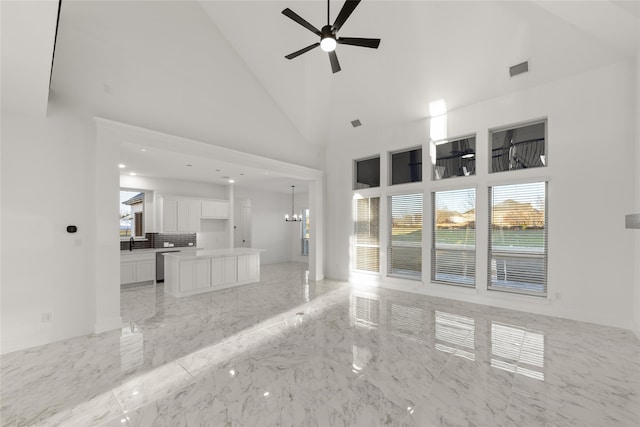 unfurnished living room featuring ceiling fan with notable chandelier and high vaulted ceiling