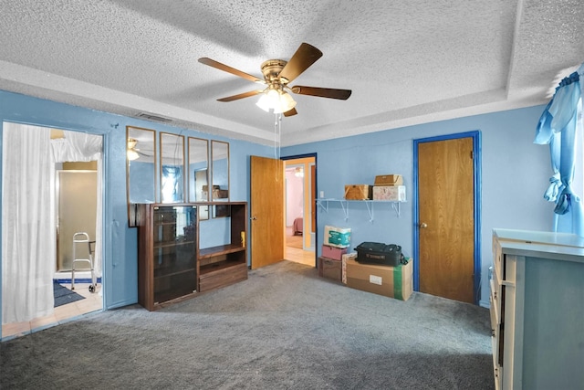 carpeted living room featuring ceiling fan, a textured ceiling, and a tray ceiling