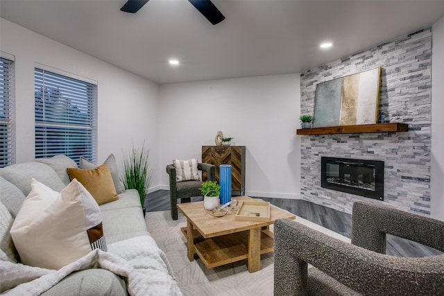 living area featuring wood finished floors, a glass covered fireplace, a ceiling fan, and baseboards