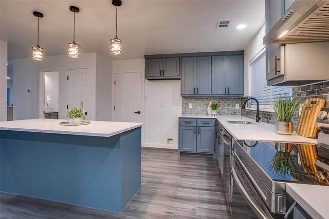 kitchen with visible vents, decorative light fixtures, ventilation hood, light countertops, and a sink