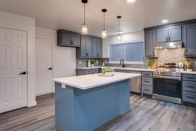 kitchen with decorative light fixtures, light countertops, appliances with stainless steel finishes, a kitchen island, and under cabinet range hood