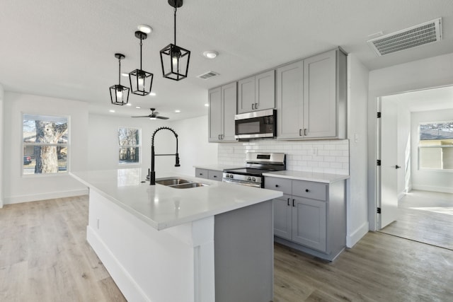 kitchen with a kitchen island with sink, visible vents, stainless steel appliances, and light countertops