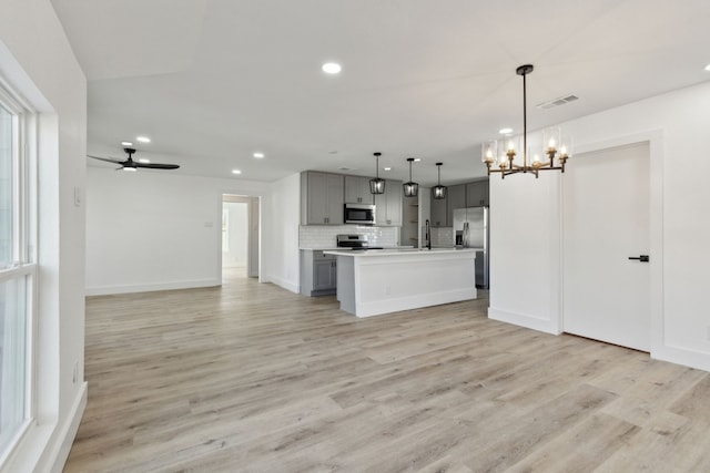 kitchen with stainless steel appliances, open floor plan, light countertops, hanging light fixtures, and gray cabinets