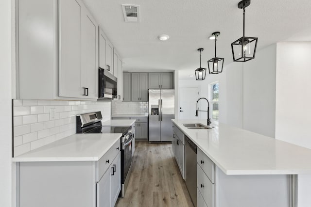 kitchen with pendant lighting, a center island with sink, light countertops, appliances with stainless steel finishes, and a sink