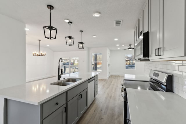 kitchen featuring gray cabinetry, a sink, light countertops, appliances with stainless steel finishes, and decorative light fixtures