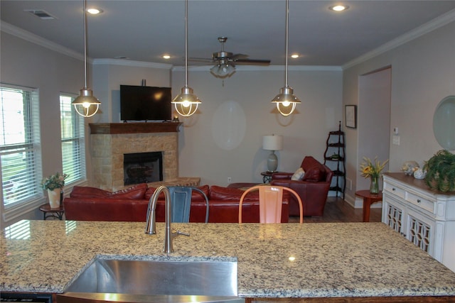 kitchen featuring pendant lighting, a fireplace, light stone countertops, and sink