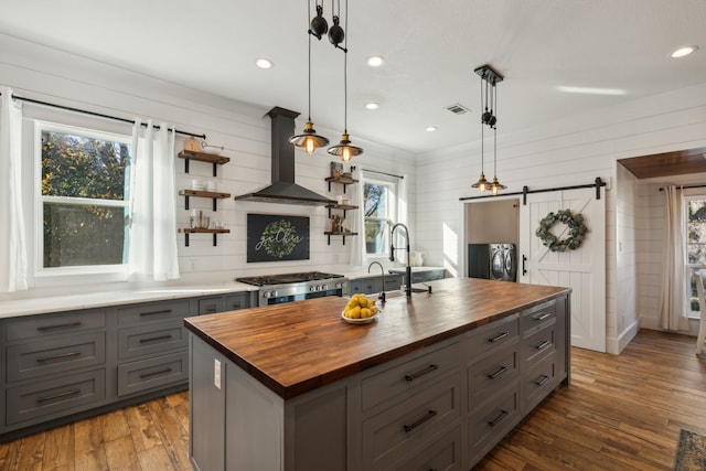 kitchen featuring wooden counters, island range hood, a barn door, decorative light fixtures, and an island with sink