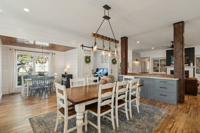 dining space with wood walls, ceiling fan, a barn door, and wood-type flooring