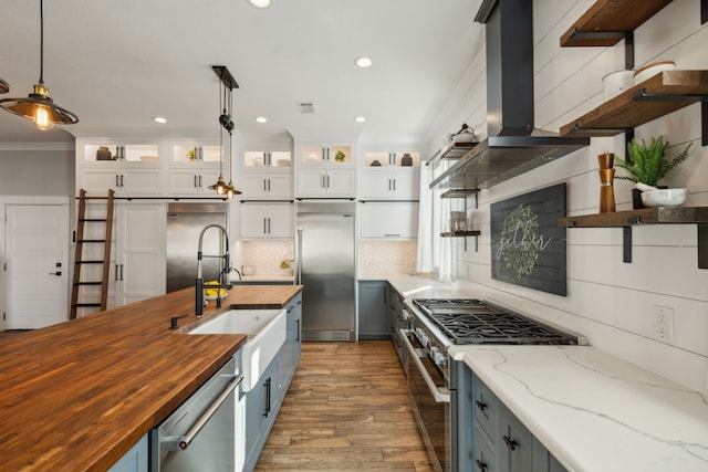 kitchen with wooden counters, island exhaust hood, high end appliances, decorative light fixtures, and white cabinetry