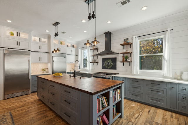 kitchen with island exhaust hood, appliances with stainless steel finishes, wooden counters, white cabinetry, and an island with sink