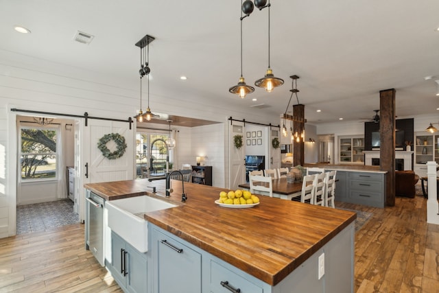 kitchen with butcher block countertops, a barn door, a kitchen island with sink, and pendant lighting