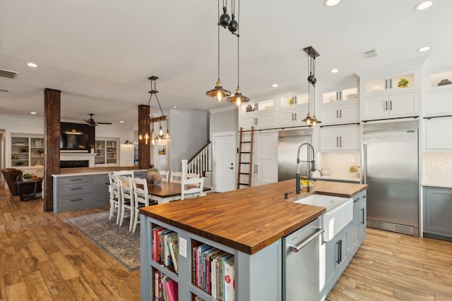 kitchen with white cabinetry, ceiling fan, stainless steel appliances, wooden counters, and a center island with sink