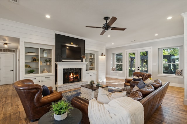 living room featuring french doors, hardwood / wood-style flooring, ceiling fan, ornamental molding, and a large fireplace