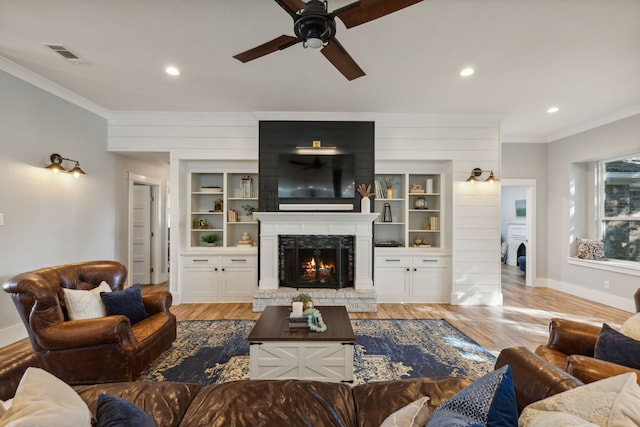 living room with crown molding, ceiling fan, built in features, a fireplace, and light hardwood / wood-style floors