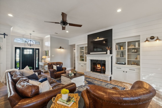 living room with ceiling fan with notable chandelier, light hardwood / wood-style floors, wooden walls, and built in shelves