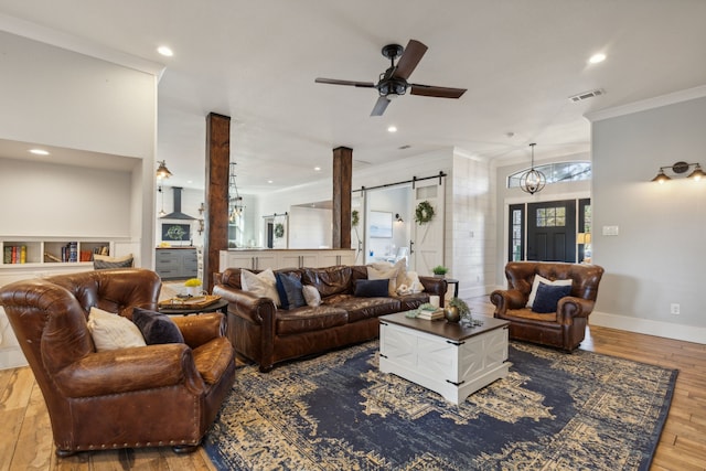 living room featuring a barn door, crown molding, ceiling fan with notable chandelier, and light wood-type flooring