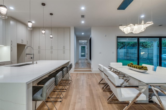 kitchen featuring a kitchen island with sink, sink, pendant lighting, light hardwood / wood-style flooring, and white cabinetry