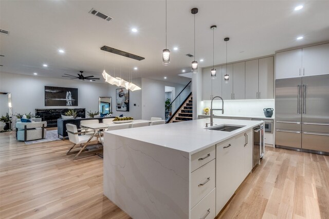 kitchen featuring stainless steel built in fridge, white cabinets, pendant lighting, and a center island with sink