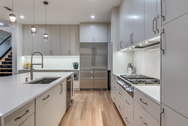 kitchen featuring light wood-type flooring, stainless steel appliances, sink, decorative light fixtures, and white cabinetry