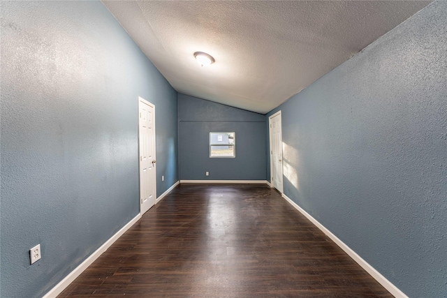 unfurnished room featuring dark hardwood / wood-style flooring, a textured ceiling, and vaulted ceiling