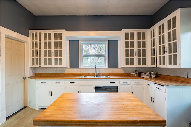 kitchen with tasteful backsplash, sink, light tile patterned floors, white cabinets, and butcher block countertops