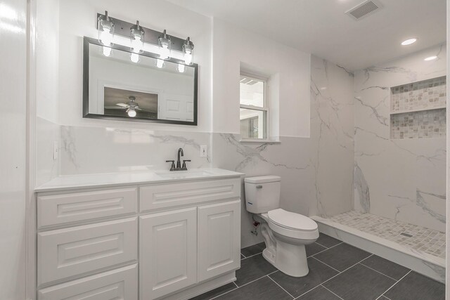 bathroom featuring a tile shower, ceiling fan, toilet, vanity, and tile walls