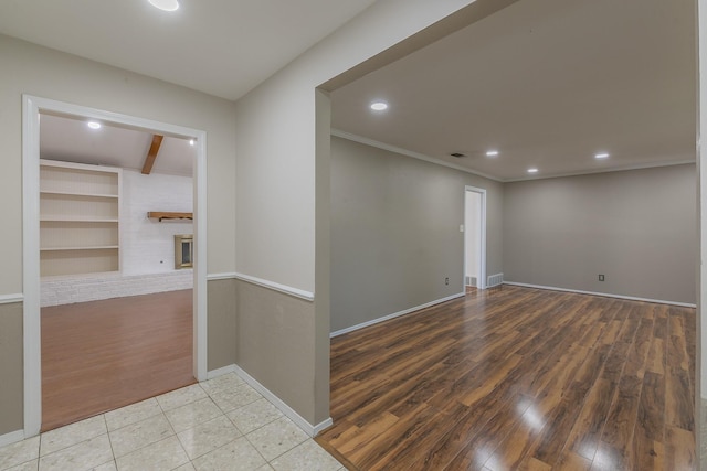 spare room with built in shelves, ornamental molding, a fireplace, beamed ceiling, and light hardwood / wood-style floors