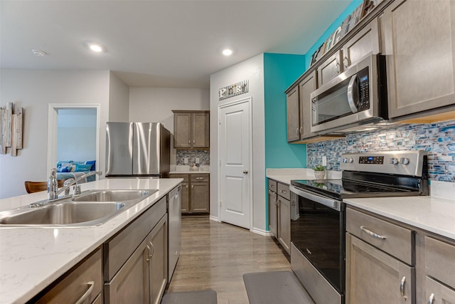 kitchen with light stone countertops, tasteful backsplash, stainless steel appliances, sink, and wood-type flooring