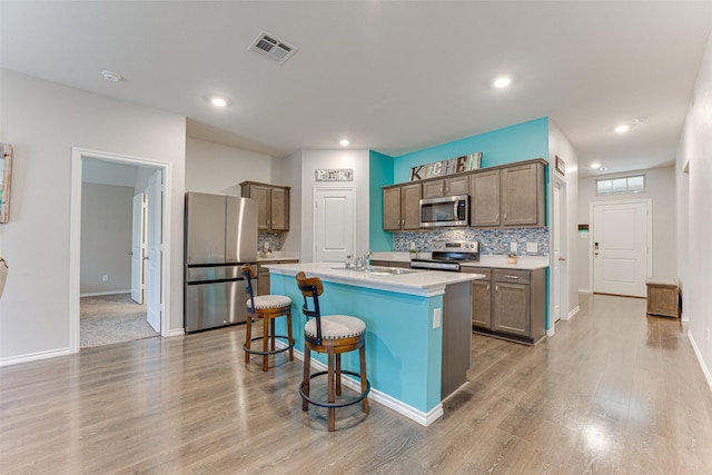 kitchen featuring a kitchen bar, tasteful backsplash, stainless steel appliances, a center island with sink, and light hardwood / wood-style flooring